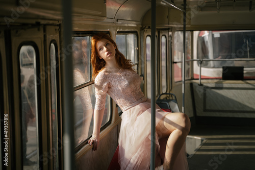 Beautiful red haired young girl in retro style lace fancy dress. Public transport fashion mood. romantic melancholy nostalgia emotions portrait pensive girl in old tram looks through the window. 