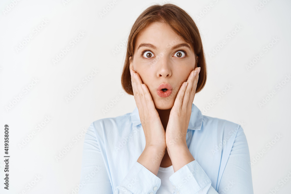 Wow amazing. Close up portrait of impressed and surprised young woman look at camera excited with opened mouth, holding hands on cheeks, checking out promo, white background Wow amazing. Close up portrait of impressed and surprised young woman look at camera excited with opened mouth, holding hands on cheeks, checking out promo, white background