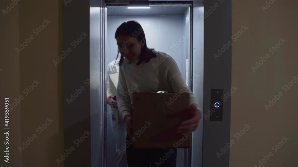 Young couple getting out of the elevator with cardboard boxes moving in to new appartment Young couple getting out of the elevator with cardboard boxes moving in to new appartment