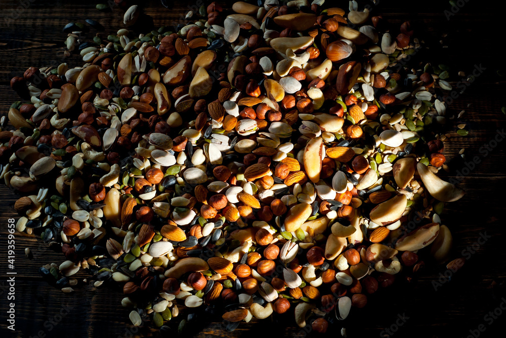 Many types of nuts close up. Textures of different nuts. Nuts are dumped in a pile. Contrasting dramatic light as an artistic effect.
