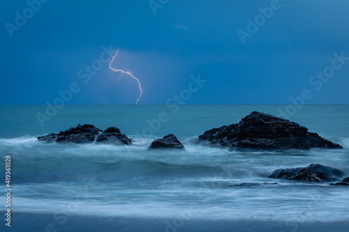 Fototapeta Mar con aguas sedosas y rayo cayendo sobre el mar, rocas