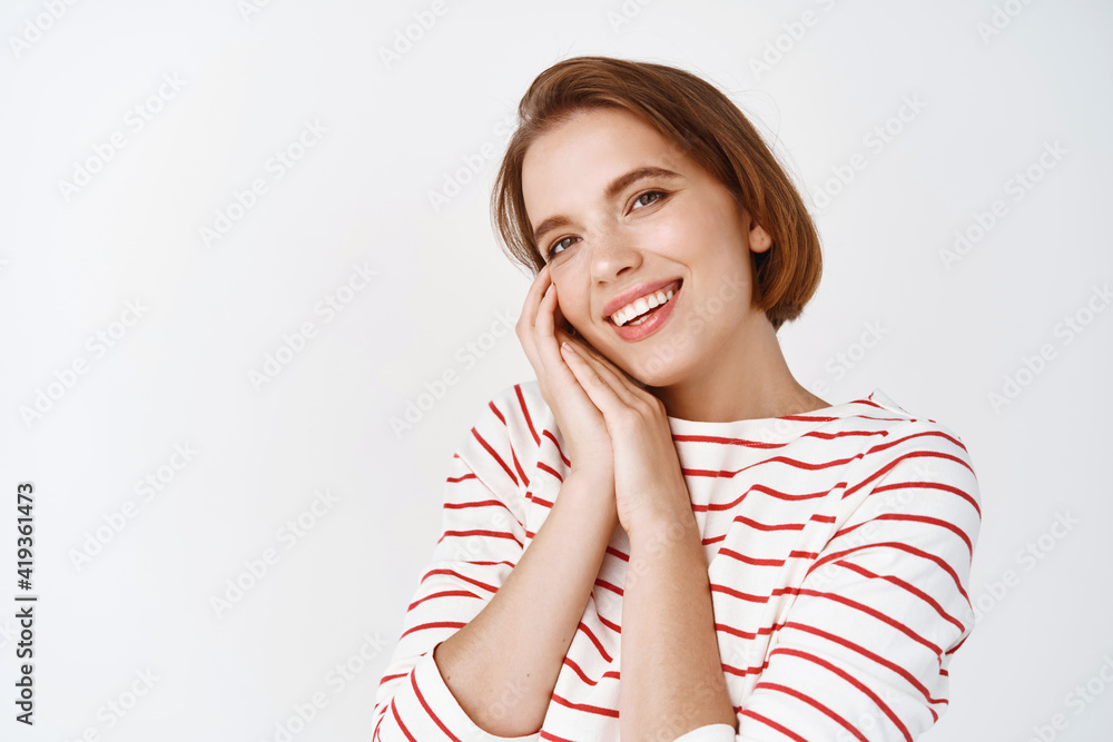 Beautiful girl with short hair and natural make-up, admire something cute, looking touched with affection, smiling at camera, standing against white background Beautiful girl with short hair and natural make-up, admire something cute, looking touched with affection, smiling at camera, standing against white background