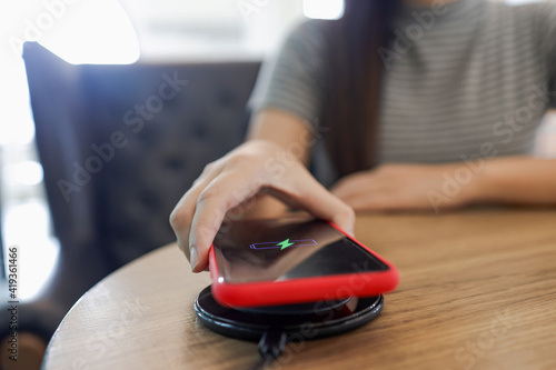 Charging mobile phone battery with wireless device in the table. Smartphone charging on a charging pad. Mobile phone near wireless charger.