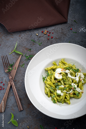 Casarecce pasta with pesto sauce, nuts and stracciatella (burrata) cheese on a white plate, close up photo