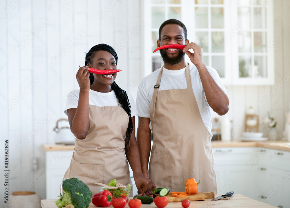 African couple having fun while cooking in kitchen, keeping pepper as moustache African couple having fun while cooking in kitchen, keeping pepper as moustache