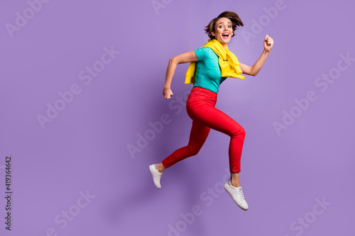 Full length photo of girl jump run open mouth wear tied sweater t-shirt pants sneakers isolated purple color background © deagreez