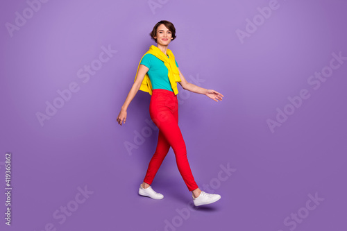 Full length photo of girl walk wear knotted pullover t-shirt pants footwear isolated violet color background