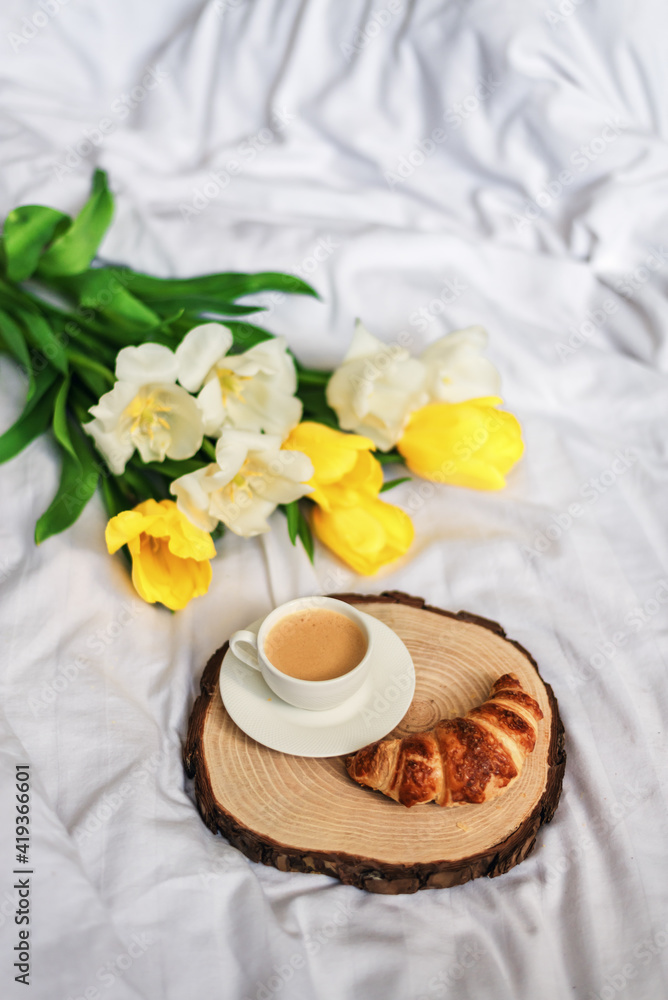 Breakfast in bed. A bouquet of tulips lies on the bed next to a cup of hot coffee. Spring. Gift. Good morning. Breakfast in bed. A bouquet of tulips lies on the bed next to a cup of hot coffee. Spring. Gift. Good morning.