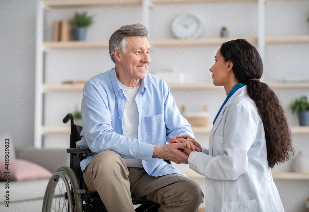 Obraz premium Older people healthcare support concept. Doctor holding hands of disabled senior man in wheelchair during medical visit