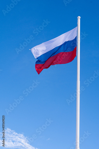 The flag of Russia waving in the wind on a long flagpole against the blue sky