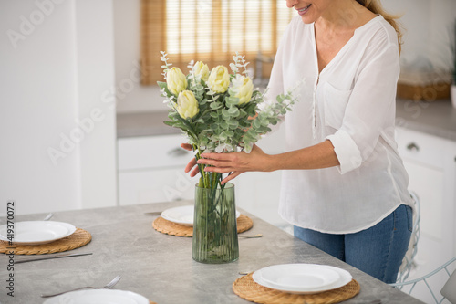 Blonde housewife in jeans putting flowers into the vase photo