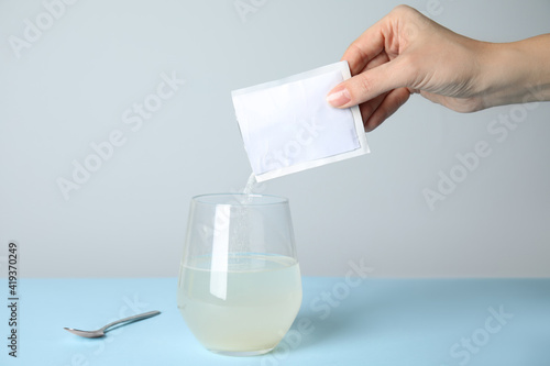 Foto Woman pouring powder from medicine sachet into glass of water on turquoise table