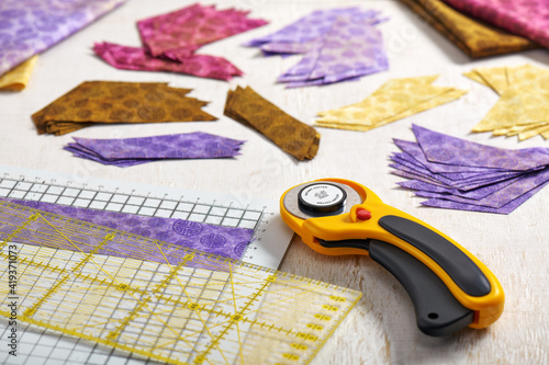 Stacks of multi-colored pieces of fabric, cutting mat, ruler, rotary cutter on a white surface