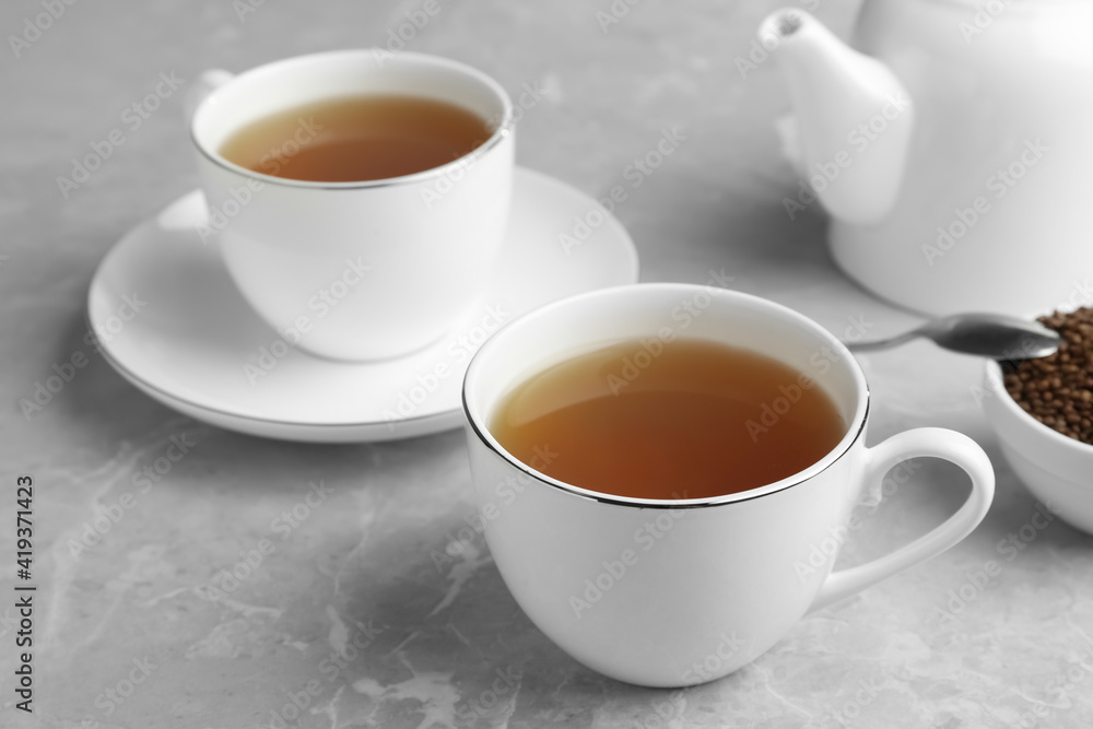 Cups of buckwheat tea and granules on light grey marble table Cups of buckwheat tea and granules on light grey marble table