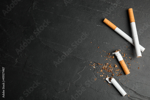 Broken and whole cigarettes on black table, flat lay with space for text. Quitting smoking concept