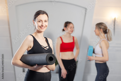 Yoga instructor posing with yoga mat. Two girls chatting in the background.