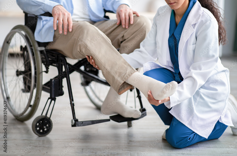 Cropped view of young doctor checking disabled senior patient's leg during medical visit at home Cropped view of young doctor checking disabled senior patient's leg during medical visit at home