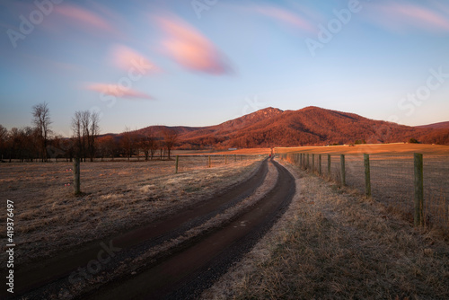 Morning light illuminating Old Rag Mountain of Shenandoah National Park as a man looks on down the dirt farm road.