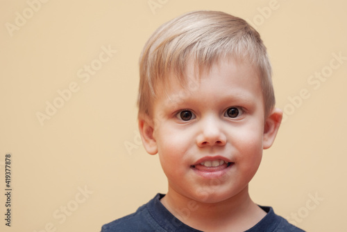 Portrait of adorable little boy with brown eyes in dark outfit posing for camera on beige background in studio close view