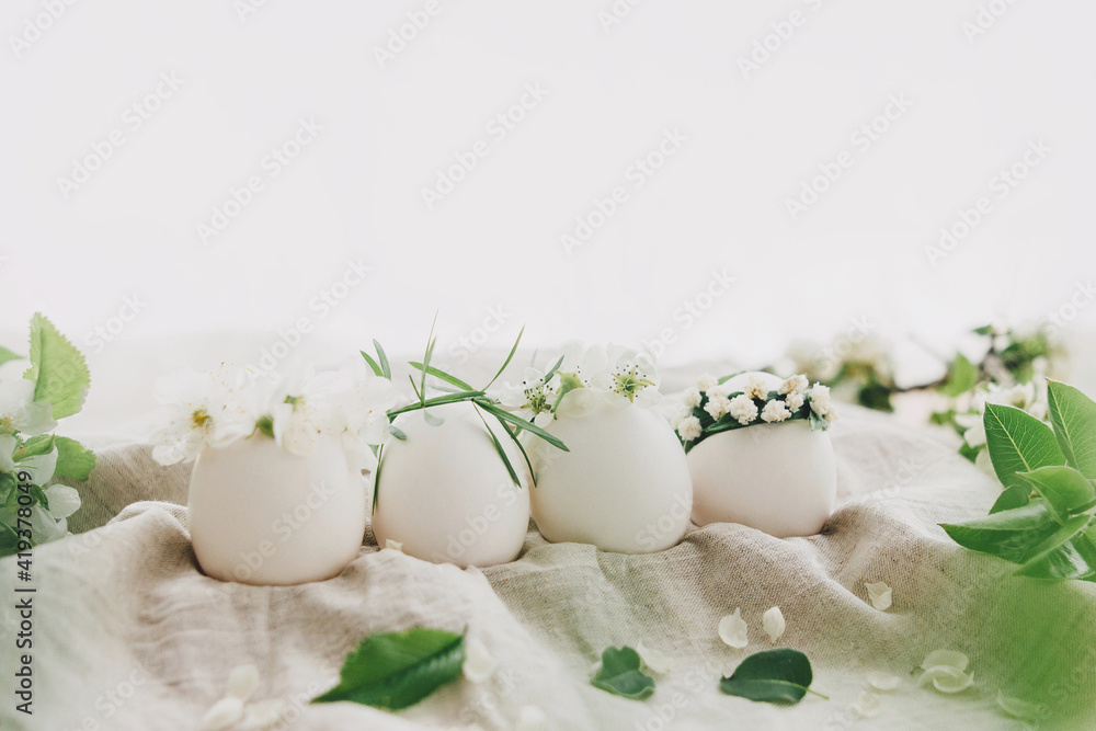 Natural easter eggs in cute floral wreaths on linen fabric with blooming spring branch and petals Natural easter eggs in cute floral wreaths on linen fabric with blooming spring branch and petals