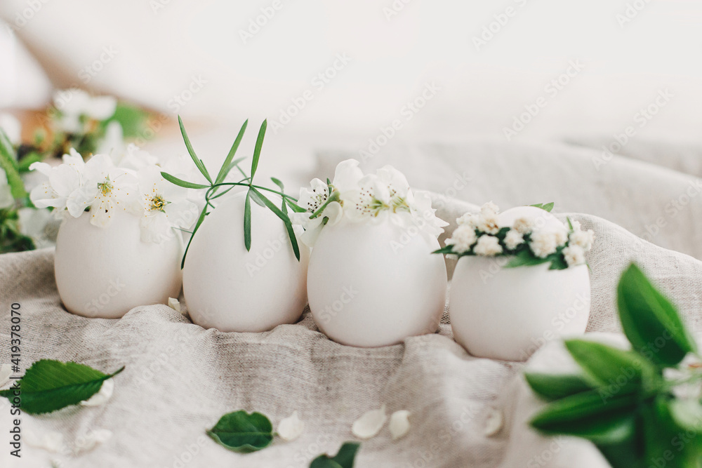 Natural easter eggs in floral crowns on linen fabric with blooming spring branch and white petals