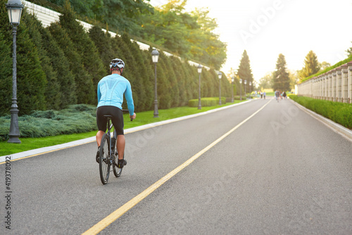 Full length shot of professional road bicycle racer in sportswear and protective helmet training in the park at sunset