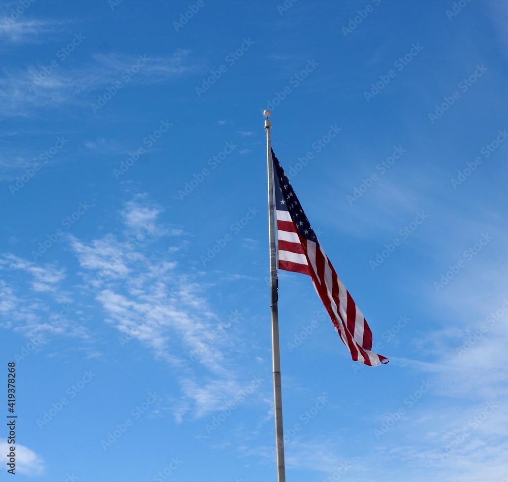 The american flag with the blue sky and clouds .