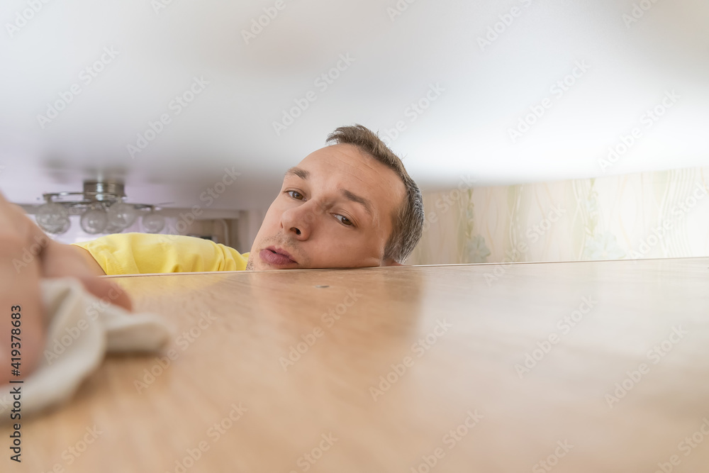 Concept of cleaning the house. a man wipes dust from a tall cabinet in his house. he goes up to the ceiling and runs a rag over the dusty cabinet.