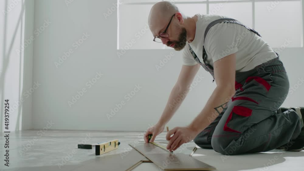 Worker measures parquet board makes mark sitting on floor Worker measures parquet board makes mark sitting on floor