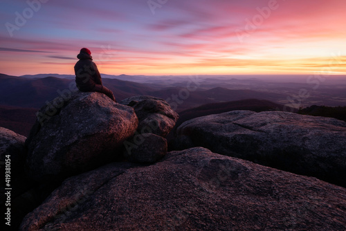 A man enjoys the colorful sunrise atop the summit of Old Rag Mountain in Shenandoah National Park.