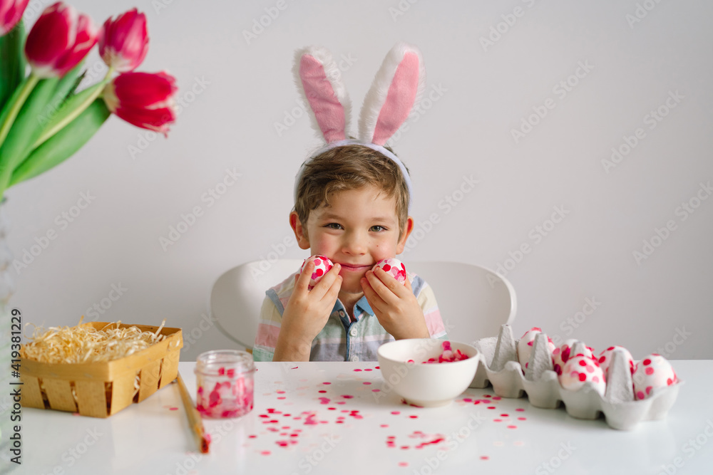 A little boy in bunny ears decorates Easter eggs. Easter concept A little boy in bunny ears decorates Easter eggs. Easter concept