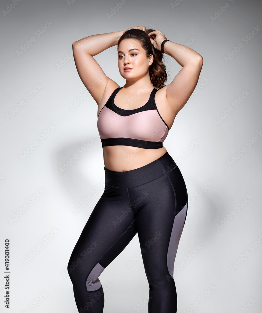 Ready to workout. Photo of model with curvy figure in fashionable sportswear on grey background. Sports motivation and healthy lifestyle