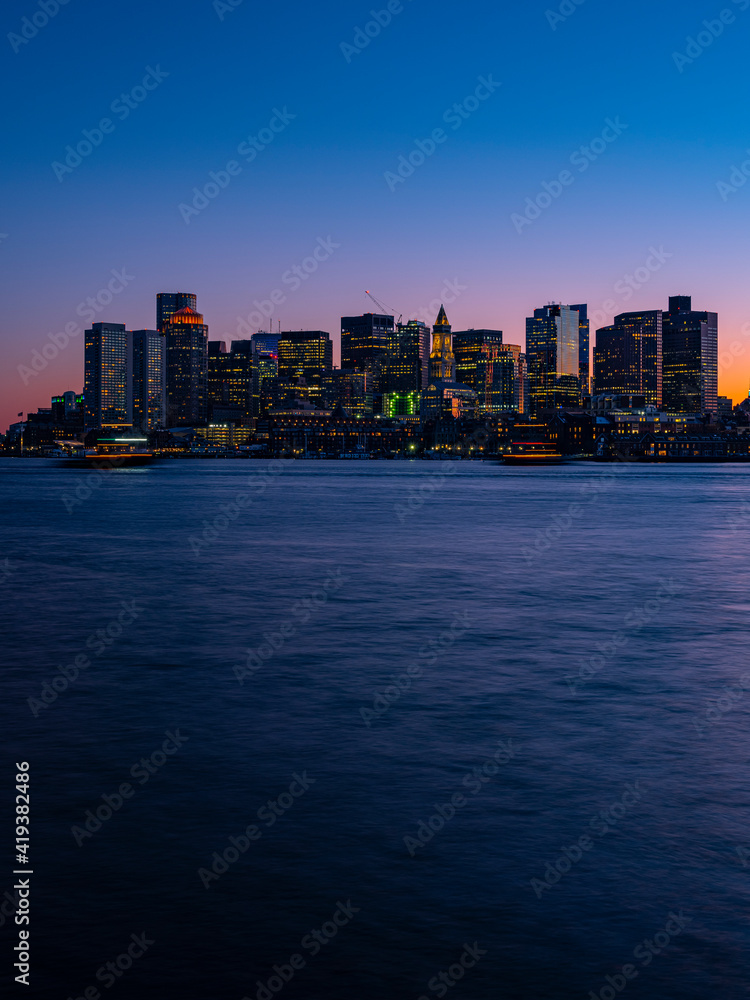 Tall Boston Skyline over Mystic River at Twilight. Modern City of Boston Long Exposure Photo with Soft Flowing River Water and Clear Blue and Pink Sky.