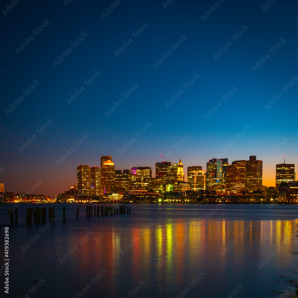 Boston Nightscape Skyline and Water Light Reflections on Mystic River. The Modern City of Boston and Weathered Damaged Dock Pilings. Harmony of Nature, Civilization, and Passage of Time.