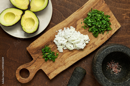 Preparing classic guacamole dish with fresh ingredients: hass avocado, onion, coriander, chili pepper, salt.