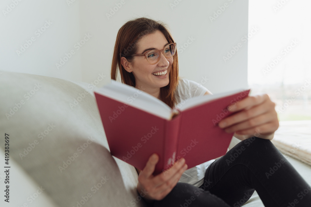 Laughing young woman relaxing at home with a book to read Laughing young woman relaxing at home with a book to read