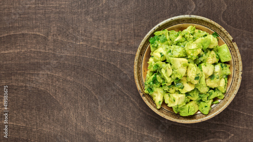 Bowl of freshly made chunky guacamole on brown wooden background with copy space for text.