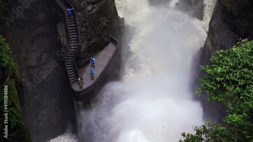 A Wild Roaring River Races Between Sheer Cliff Faces Under A Winding Stair And Platform On Which People Stand