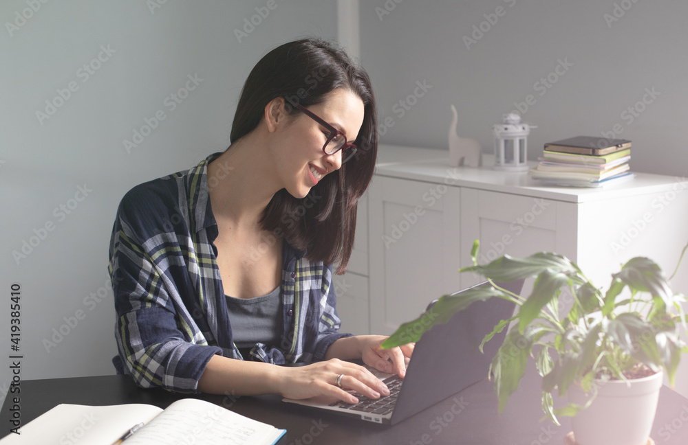 Smiling young woman freelancer using her laptop for studying and working online from home enjoying comfortable telework from home office. Self-employment and freelance concept Smiling young woman freelancer using her laptop for studying and working online from home enjoying comfortable telework from home office. Self-employment and freelance concept