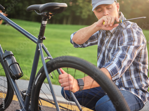 Young caucasian man holding a screwdriver while checking and repairing his bike in the public park