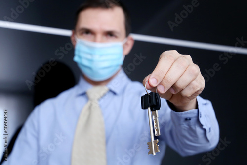 Real estate agent, apartment keys in male hands. Man in medical face mask and office clothes, concept of purchase or rental home during coronavirus pandemic