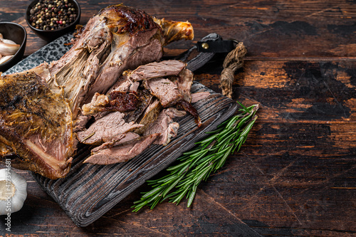 Baked lamb mutton cutting shoulder meat on a wooden board. Dark wooden background. Top view. Copy space