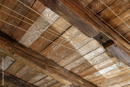 Stary strych. Dach z drewnianych belek i desek. Sznurki na bieliznę i lampa.