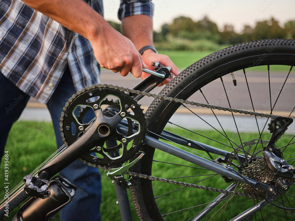 Fototapeta premium Close up shot of hands of man fixing pedals on his bike, standing in public park