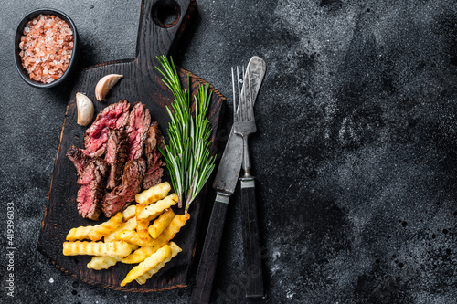 Roasted sliced machete skirt beef meat steak on wooden board with french fries. Black background. Top view. Copy space