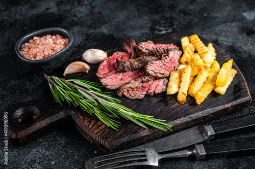 Roasted sliced machete skirt beef meat steak on wooden board with french fries. Black background. Top view