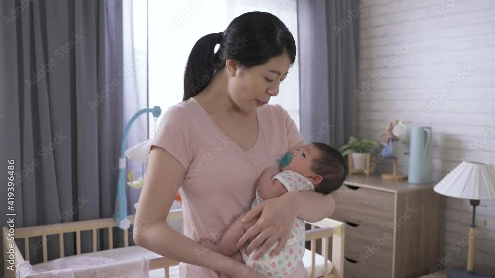 portrait happy chinese mother is smiling at her newborn child who is snuggling up close her chest by the baby cot at home. portrait happy chinese mother is smiling at her newborn child who is snuggling up close her chest by the baby cot at home.