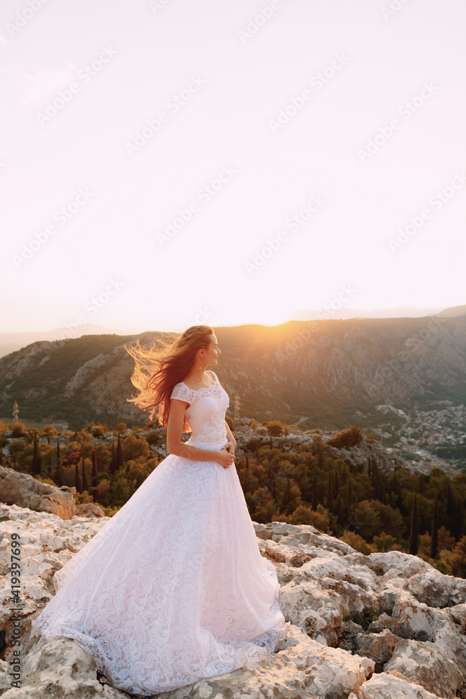 The bride in tender wedding dress stands on Mount Lovcen and looks at the Bay of Kotor 