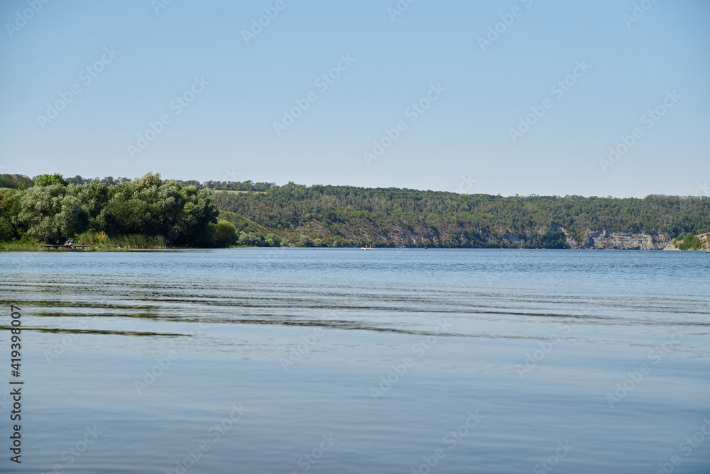 Scenic view over wide river and it's bank. Beautiful natural countryside landscape with blue sunny sky. Summer getaway vacation into isolated places. Calm water - perfect for meditation.