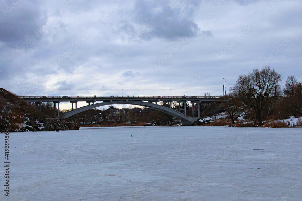 Bridge over Ros River in Bila Tserkva. Winter landscape view of frozen river in cloudy day. Bila Tserkva, Ukraine